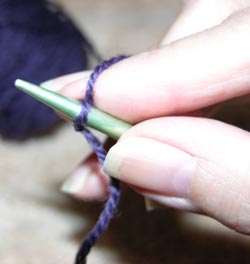 The right hand holds the knitting needle like a pencil with the index finger pressing against the stitch for control