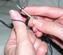 Place the yarn near the knitting needle, around and under the thumb of the left hand